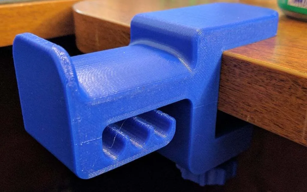 Giá treo tai nghe màu xanh in 3D kẹp bàn, giúp giải phóng không gian và giữ tai nghe an toàn.