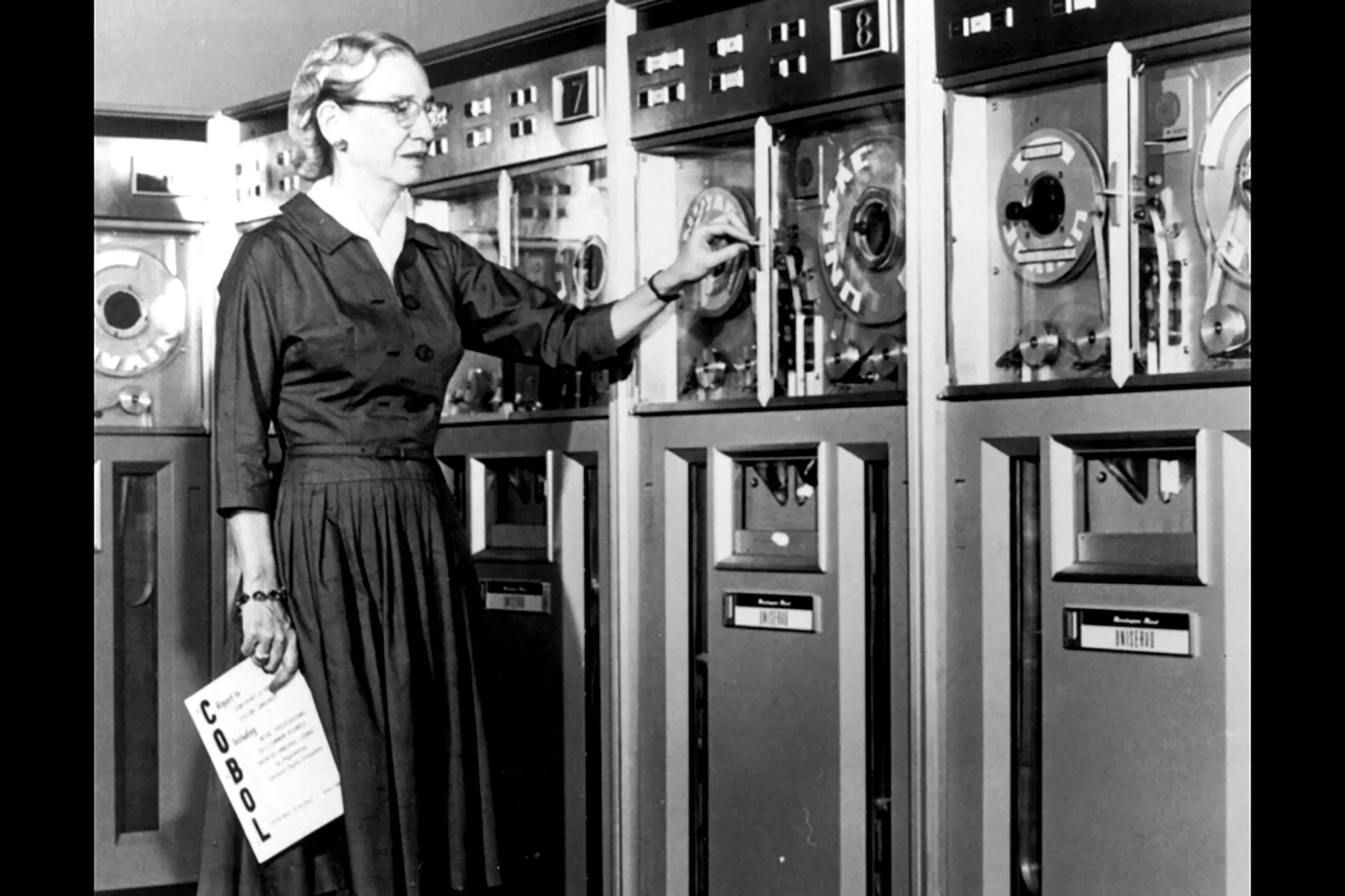 Grace Hopper cầm bản sao ngôn ngữ lập trình COBOL trước máy tính UNIVAC, biểu tượng của sự đổi mới phần mềm.