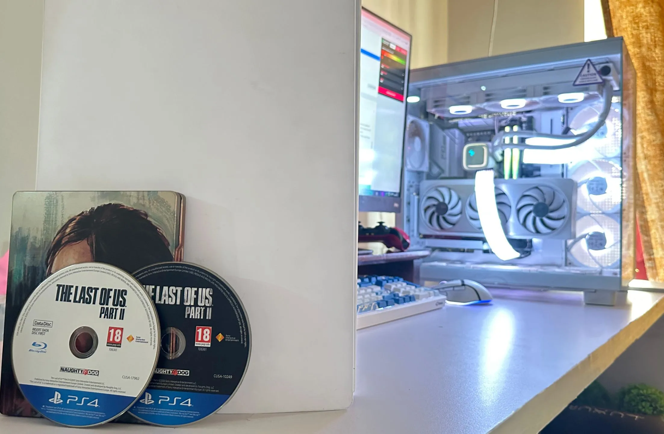 Hai đĩa game The Last of Us Part II phiên bản PS4 đặt cạnh một PC và PS5.