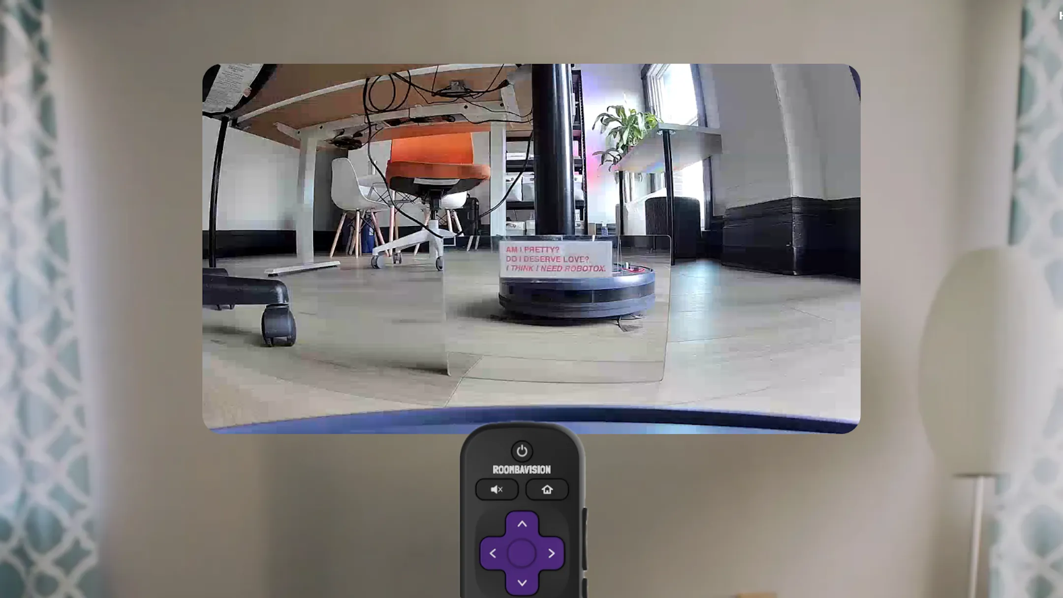Hình ảnh Roomba được trang bị camera đang đối diện với một chiếc gương, hiển thị giao diện điều khiển Roombavision trên màn hình máy tính với các nút di chuyển. Người dùng có thể điều khiển robot hút bụi từ xa để khám phá không gian ảo.