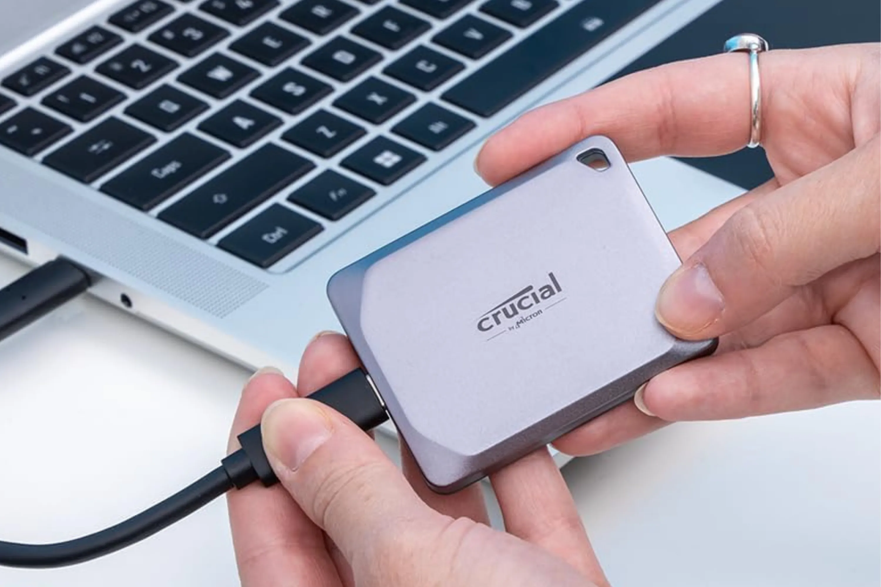 Hình ảnh SSD di động Crucial X9 Pro 4TB nằm gọn trong lòng bàn tay bên cạnh máy tính
