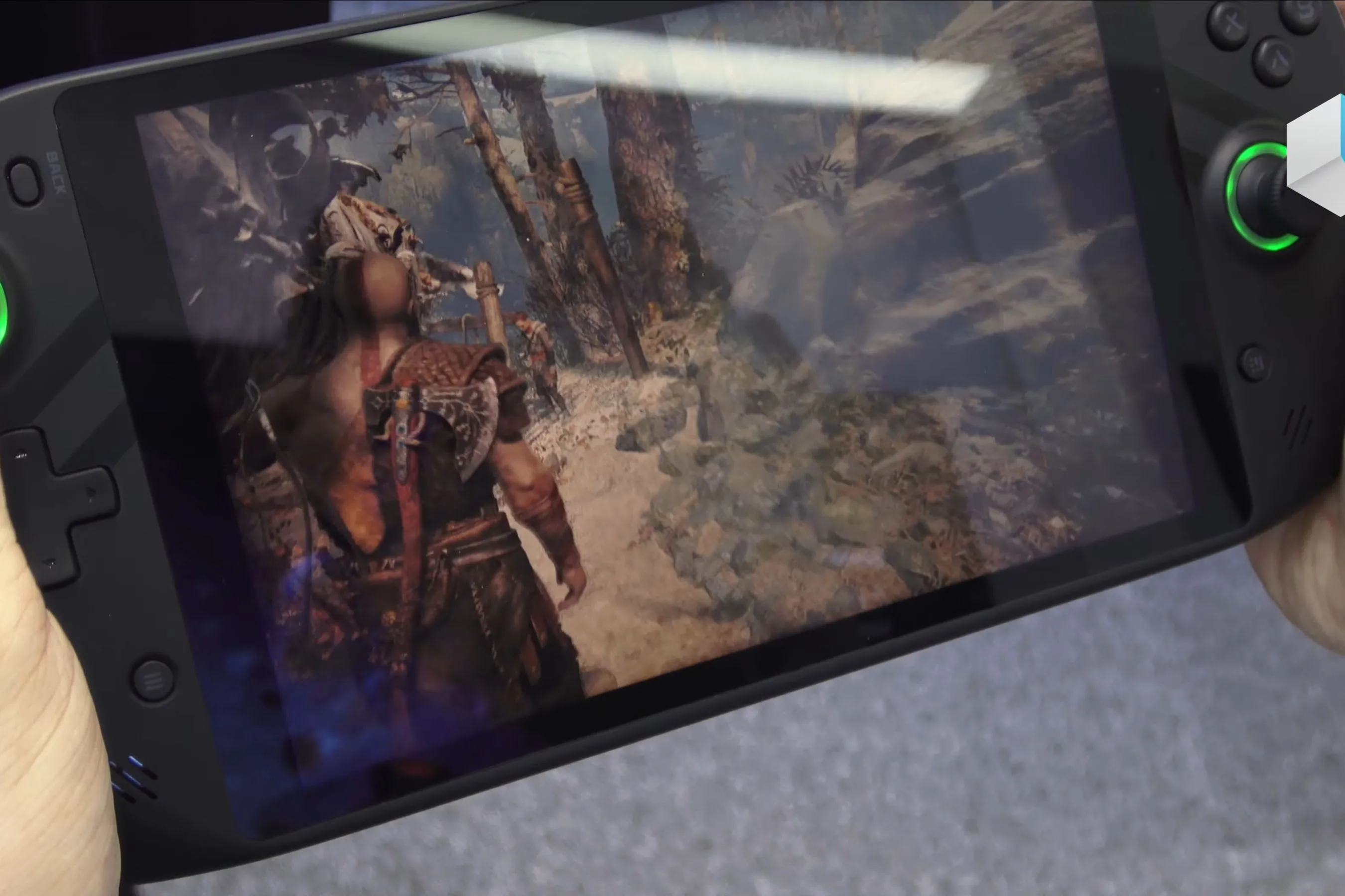 Một thiết bị chơi game cầm tay đang hiển thị tựa game God of War, cho thấy Kratos và Atreus trong cảnh chiến đấu hoành tráng, chứng minh khả năng chơi game đồ họa cao trên nền tảng di động.